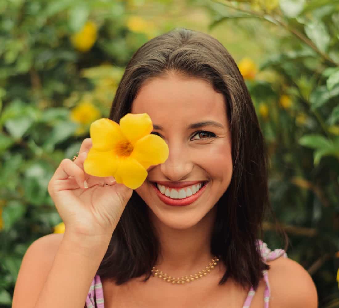Smiling woman holding a yellow flower.